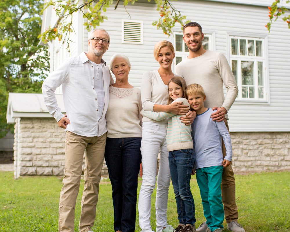 family, happiness, generation, home and people concept - happy family standing in front of house outdoors